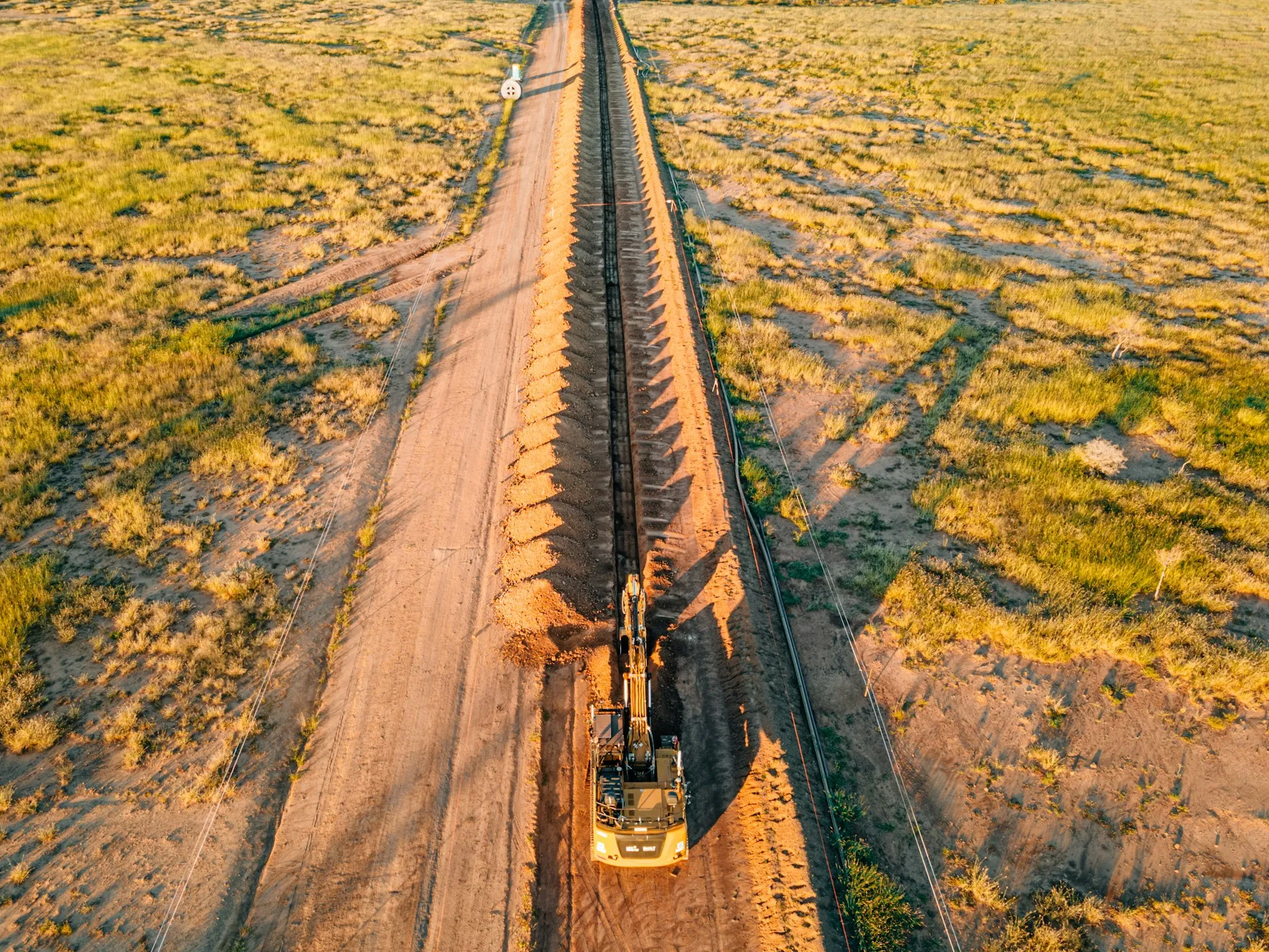Aerial view of pipeline installation with excavator working at golden hour