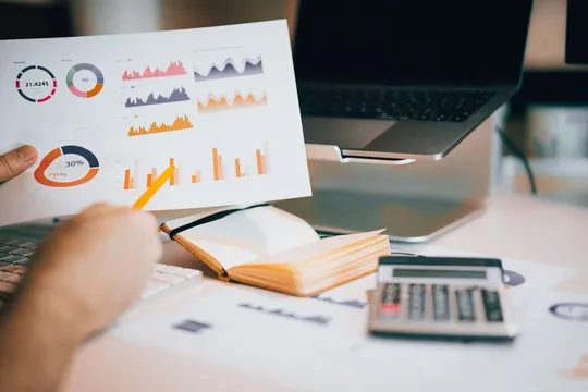 Professional reviewing financial reports and charts next to a laptop